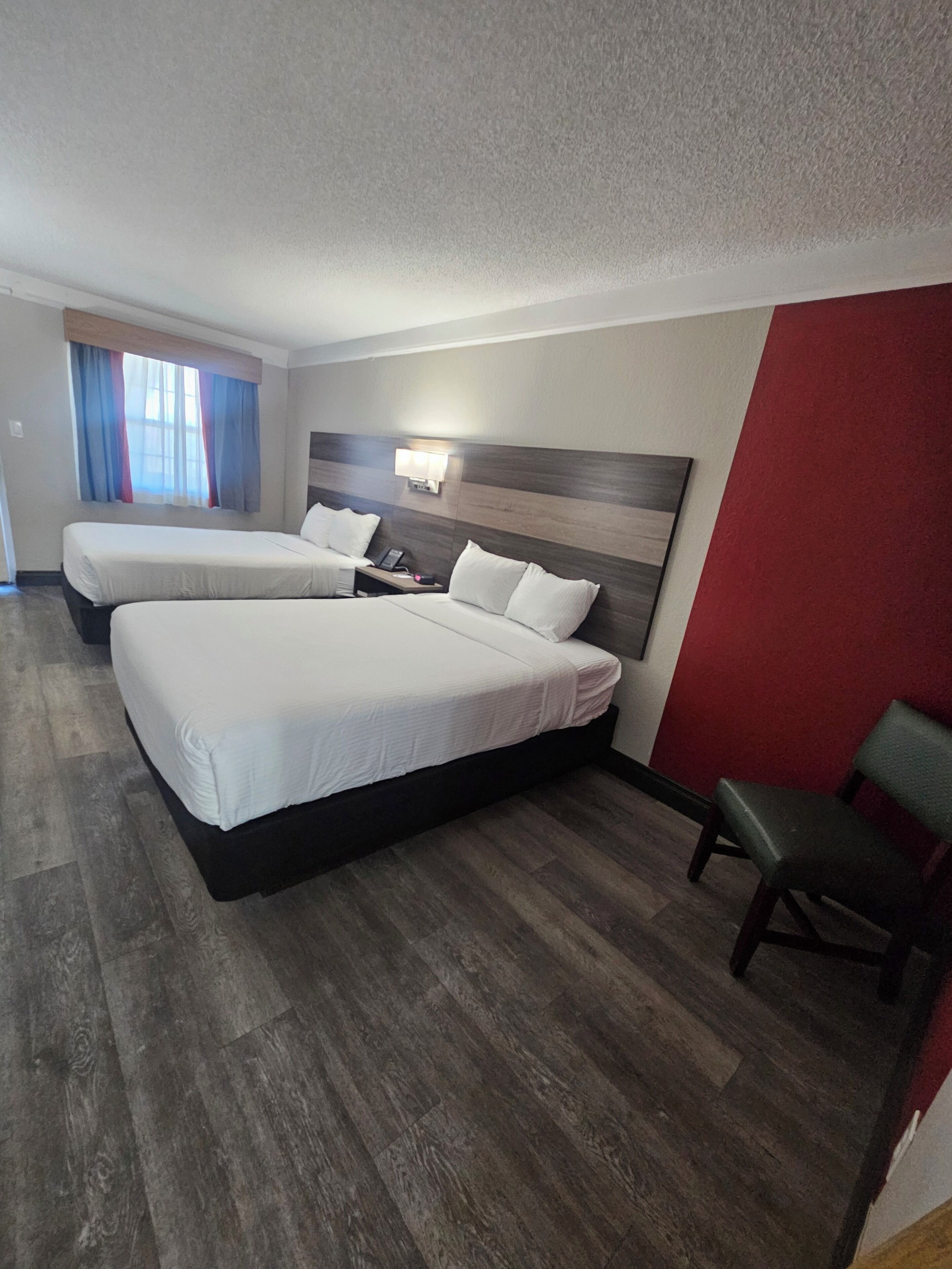 Habitación de hotel con dos camas, una pared decorada en rojo y piso de madera.