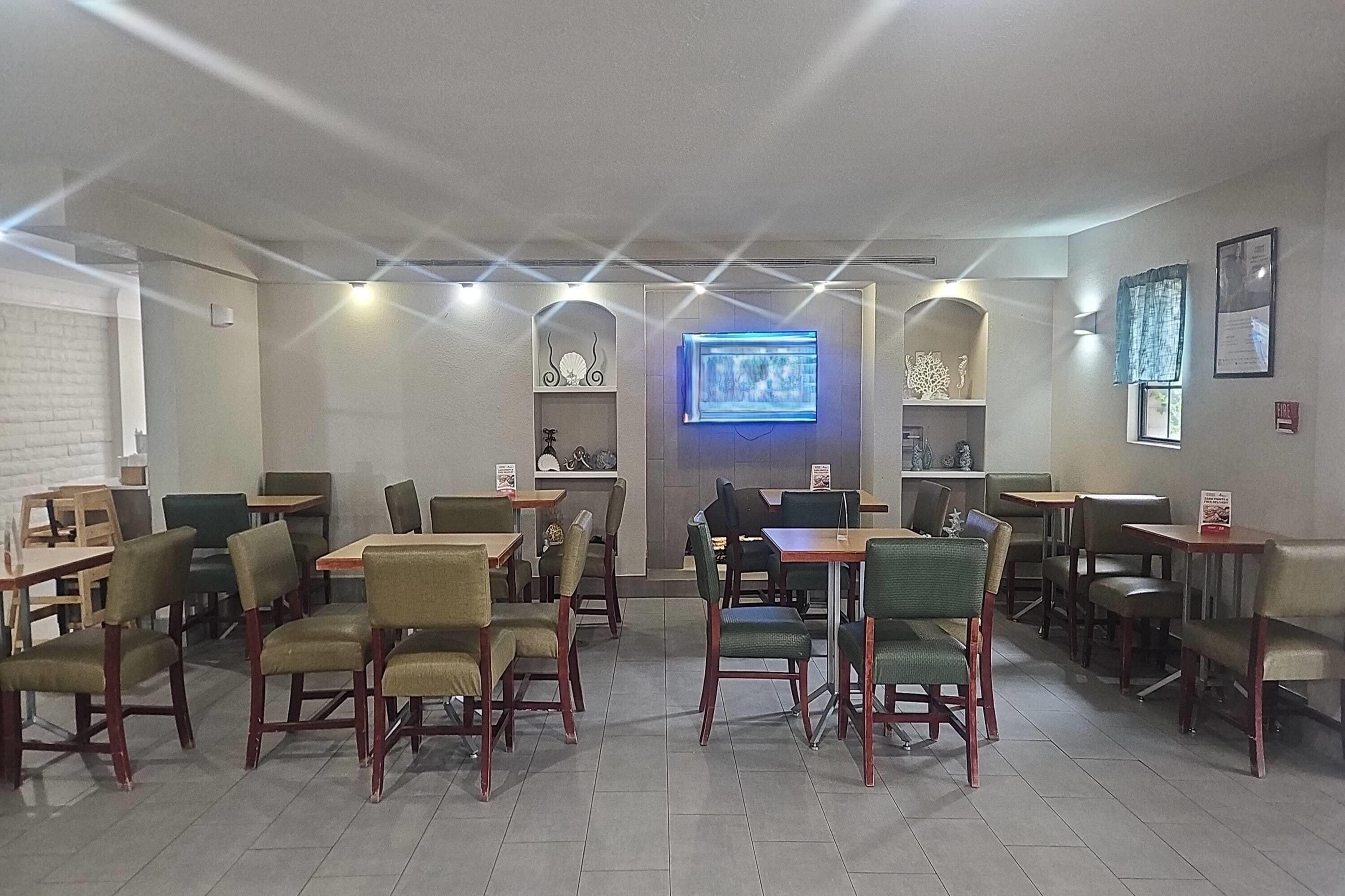 A restaurant with multiple tables and chairs, a TV screen, and a brick wall.