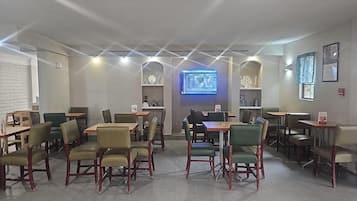 A restaurant with multiple tables and chairs, a TV screen, and a brick wall.