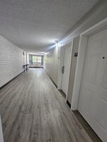 Un pasillo con piso de madera, paredes blancas y puertas a la derecha.