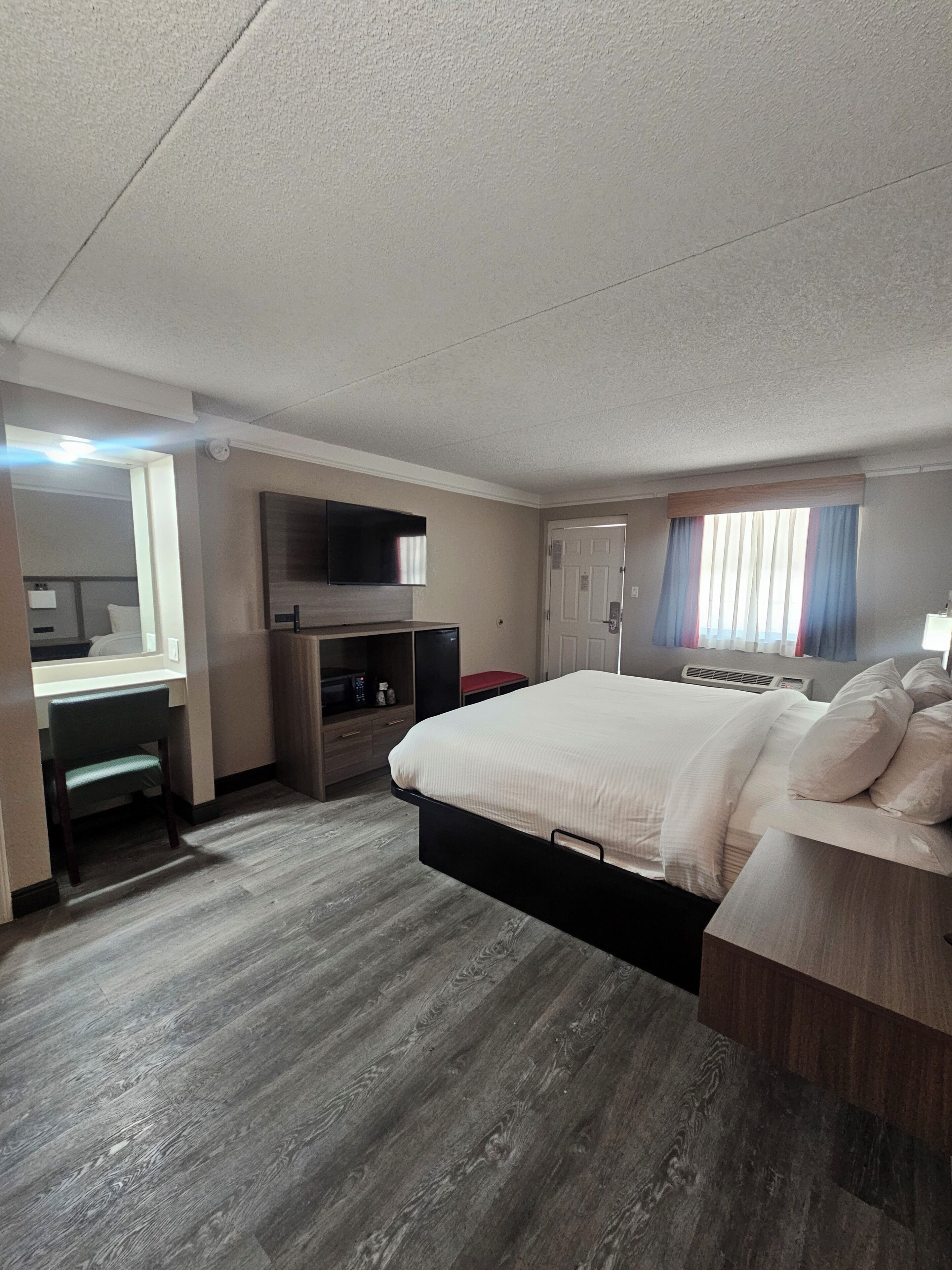 A hotel room with a bed, a desk, a television, and a window with curtains.