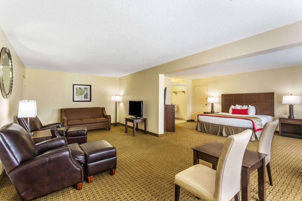 A hotel room with a sofa, armchairs, a TV, a bed, and a desk.