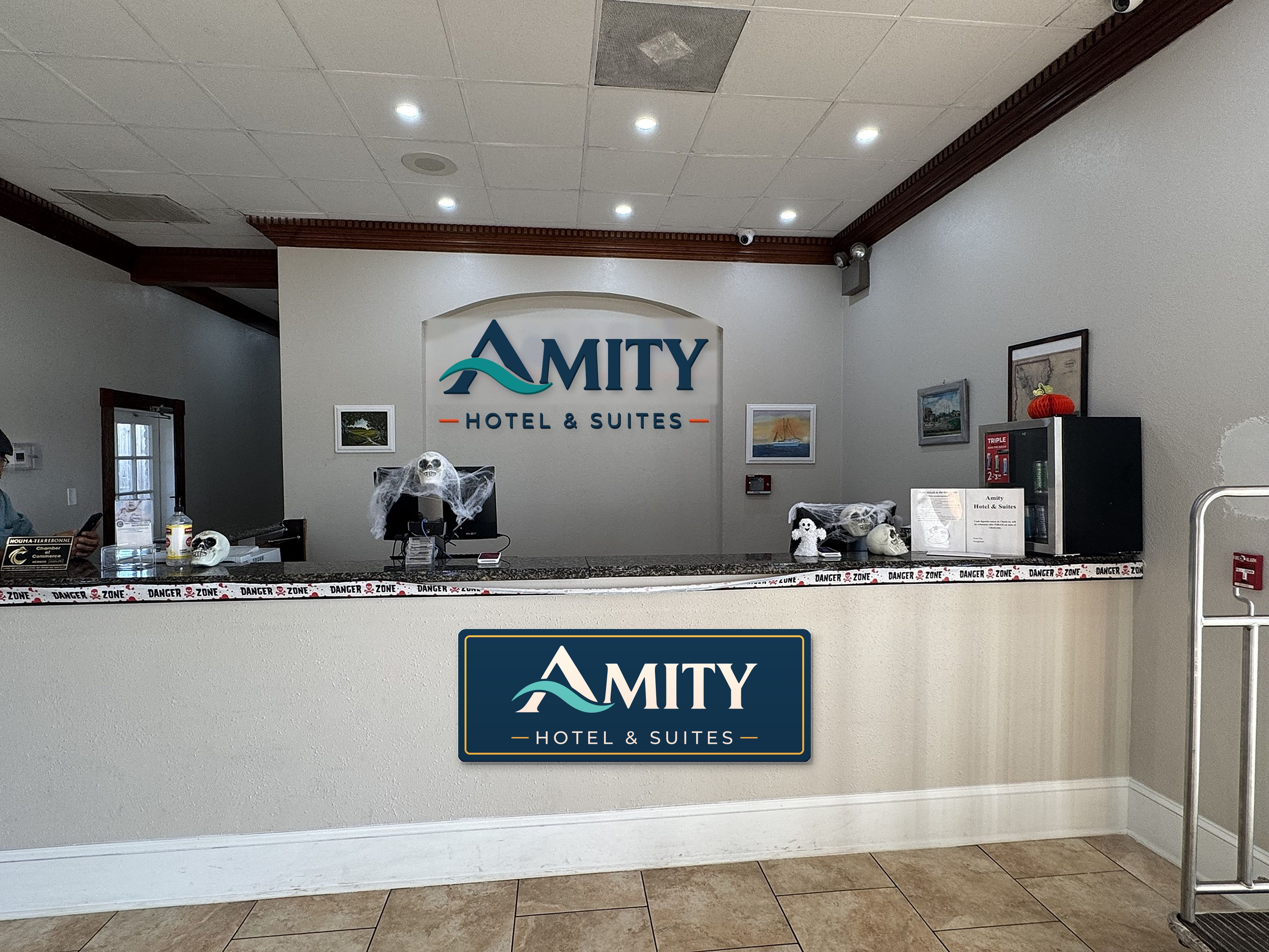 Un comptoir d’accueil avec une enseigne indiquant « AMITY HOTEL & SUITES » et un tableau encadré accroché au mur.