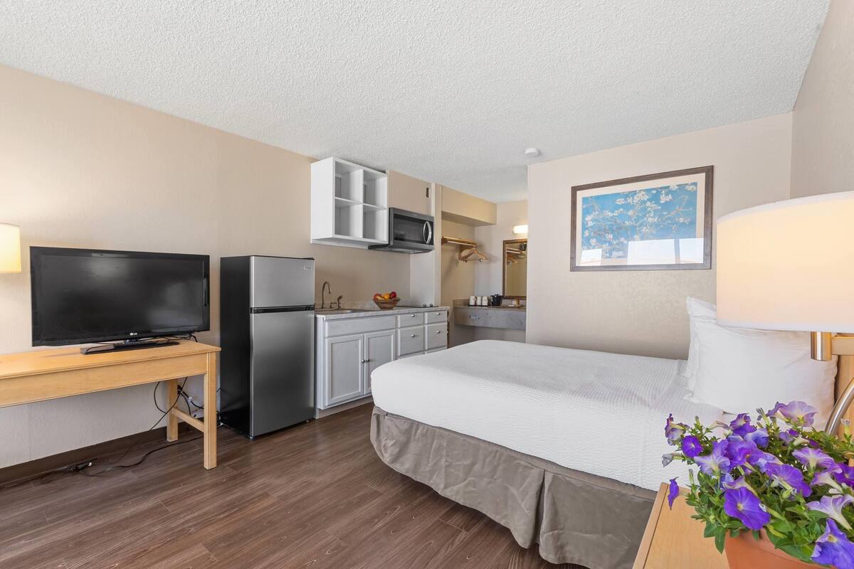 A hotel room with a bed, a TV, a kitchenette, and a bathroom.