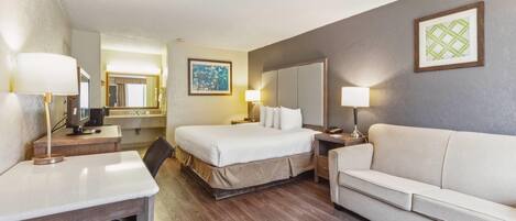 Quarto de hotel com cama, escrivaninha, cadeira, sofá, espelho e quadro na parede.