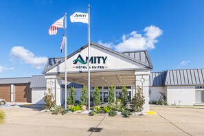 A hotel with a covered entrance, American flags, and a sign reading 'AMITY HOTEL & SUITES'. - Amity Hotel & Suites Houma (Houma)
