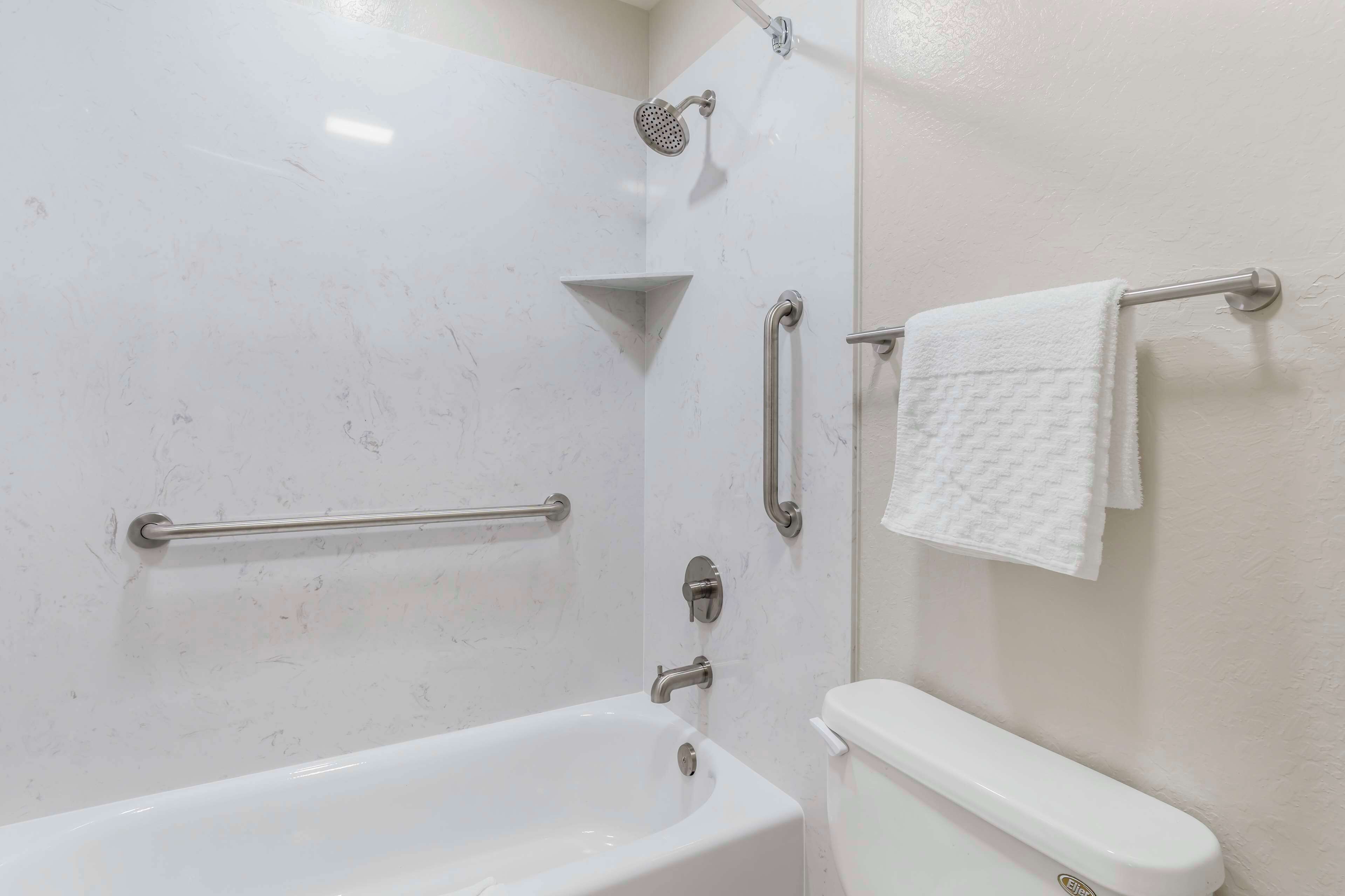 A bathroom with a bathtub, a shower, and a toilet. There are grab bars installed for safety.