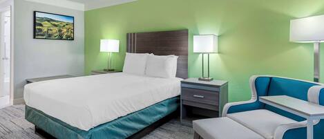 A hotel room with a bed, bedside tables, a chair, and a lamp.