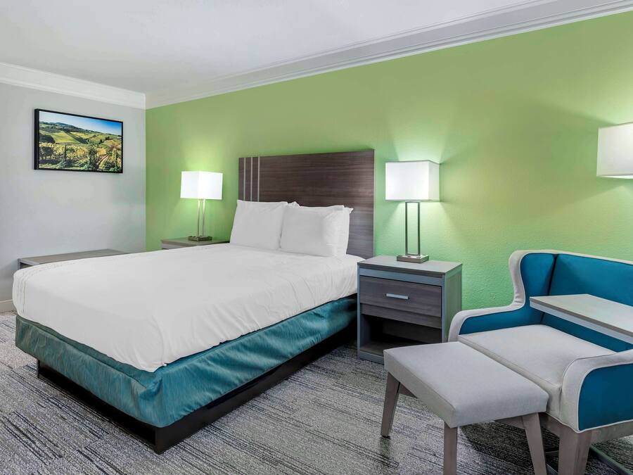 A hotel room with a bed, bedside tables, a chair, and a lamp.