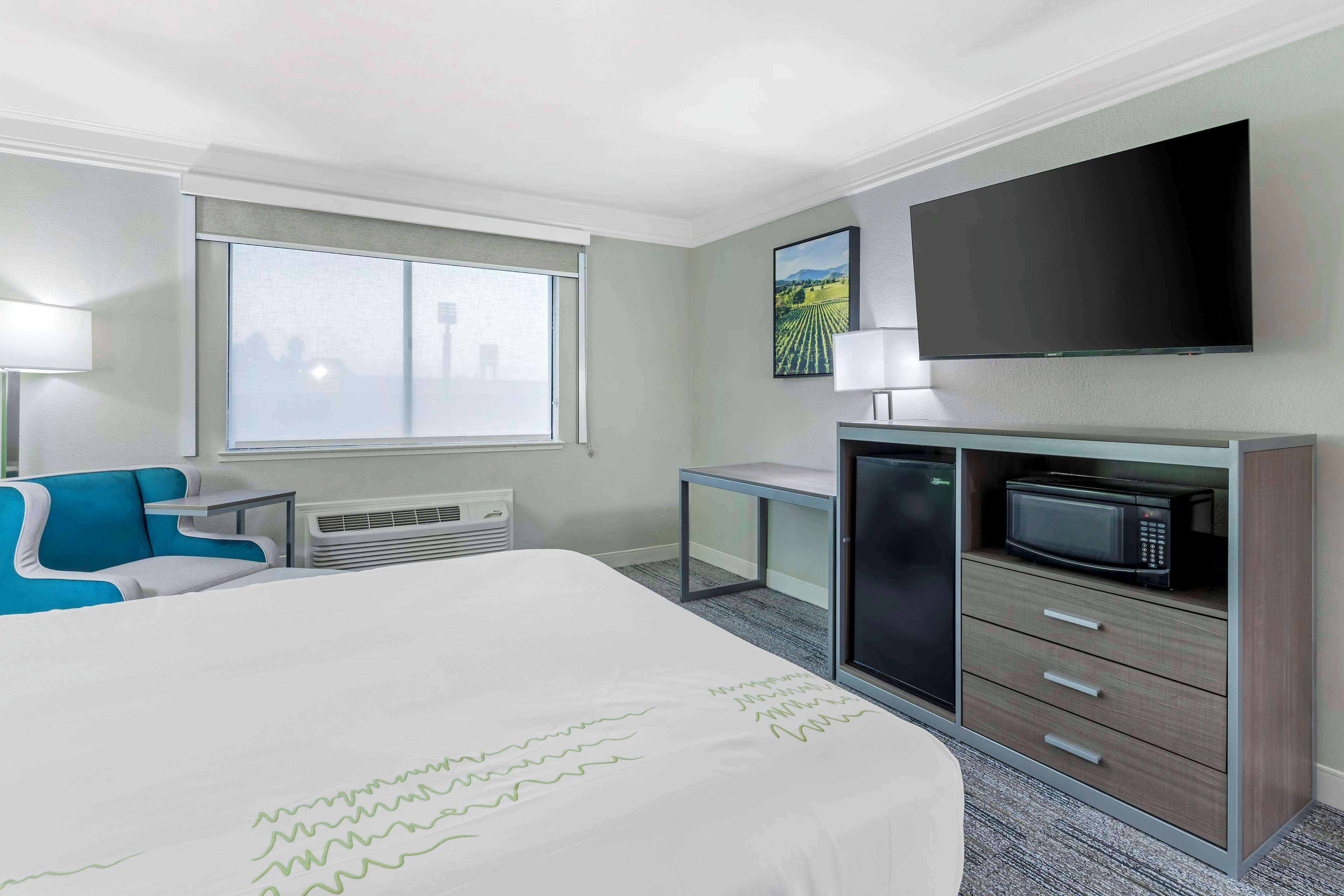 Quarto de hotel com cama, escrivaninha, televisão, micro-ondas e janela com vista para a cidade.