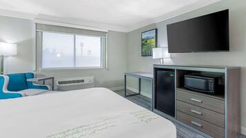 Quarto de hotel com cama, escrivaninha, televisão, micro-ondas e janela com vista para a cidade.
