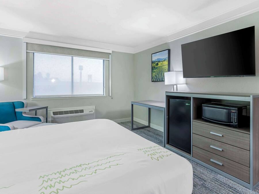 A hotel room with a bed, a desk, a television, a microwave, and a window with a cityscape view.