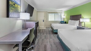 Une chambre d’hôtel avec deux lits, un bureau avec une chaise, un téléviseur fixé au mur et une fenêtre donnant sur l’extérieur.