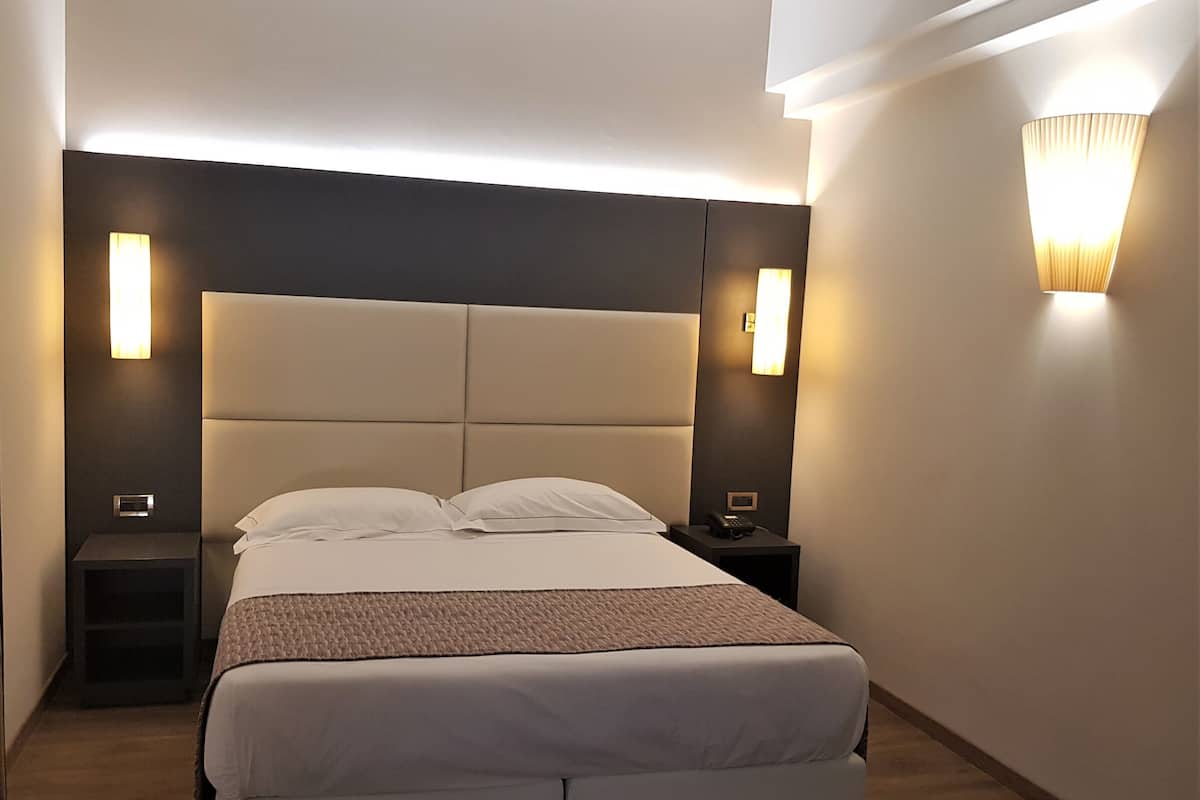 Une chambre d’hôtel moderne avec un grand lit, deux tables de chevet et des lampes fixées au mur.