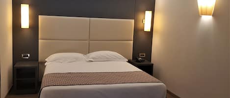 A modern hotel room with a large bed, two bedside tables, and wall-mounted lighting.