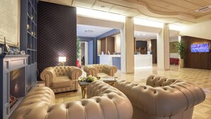 A spacious lobby with a seating area featuring tufted leather sofas and a coffee table. - Hotel Astra Ferrara (Ferrara)