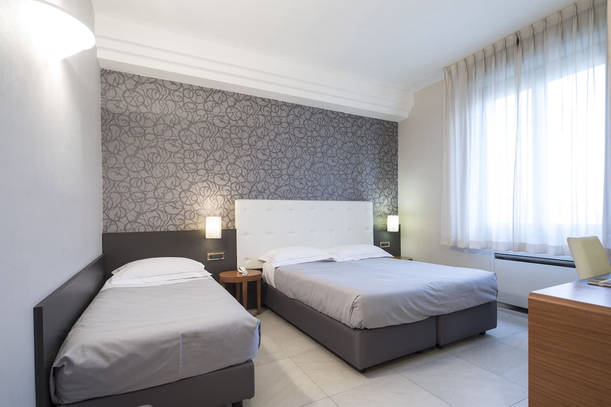 Une chambre d’hôtel avec deux lits, un bureau et une fenêtre avec des rideaux.
