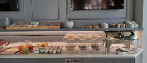 Un bufé de desayuno con diversas opciones de comida y bebidas, una máquina de café y una presentación de platos y tazas.
