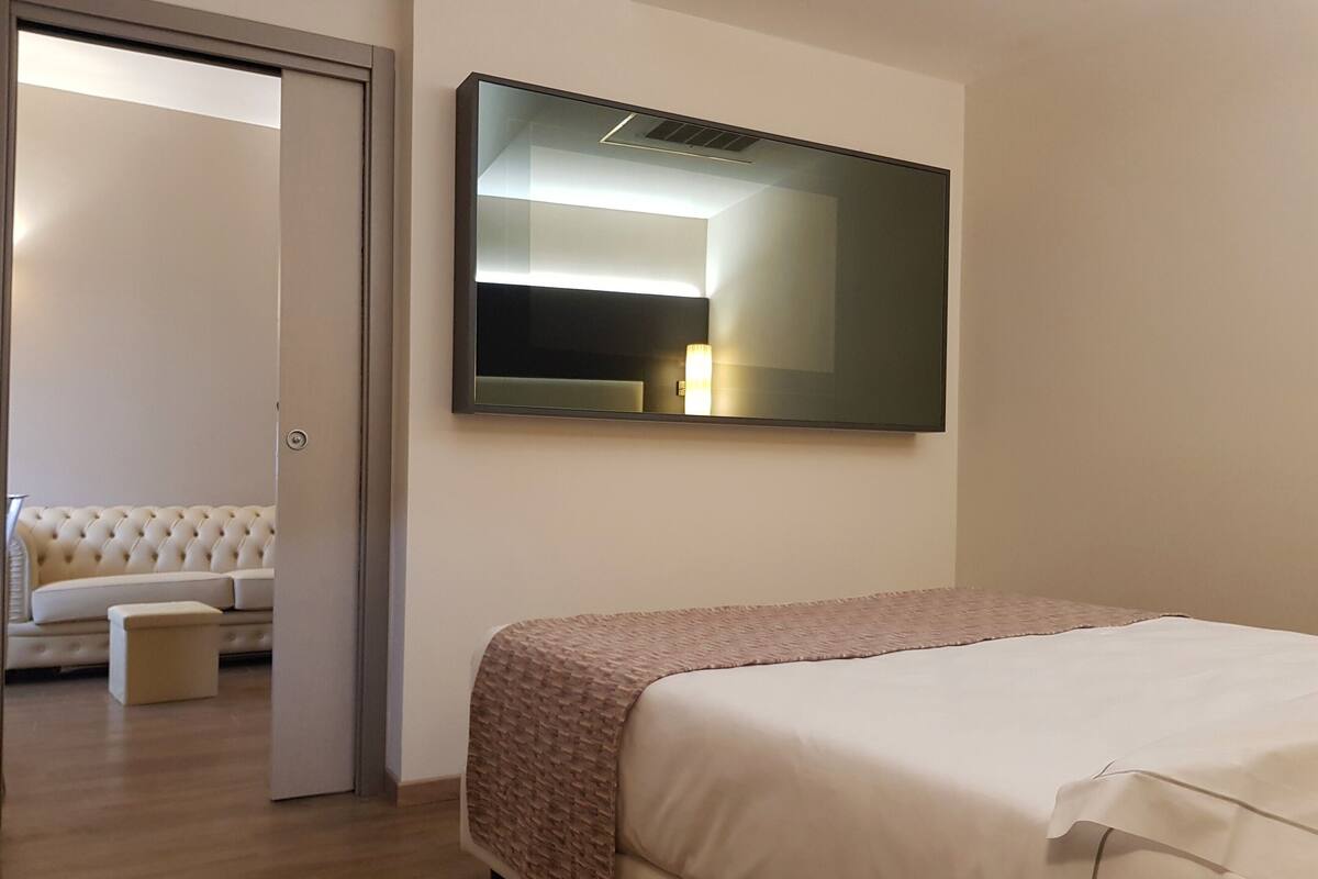 Une chambre d’hôtel avec un lit, un canapé, une petite table et un grand miroir au mur.