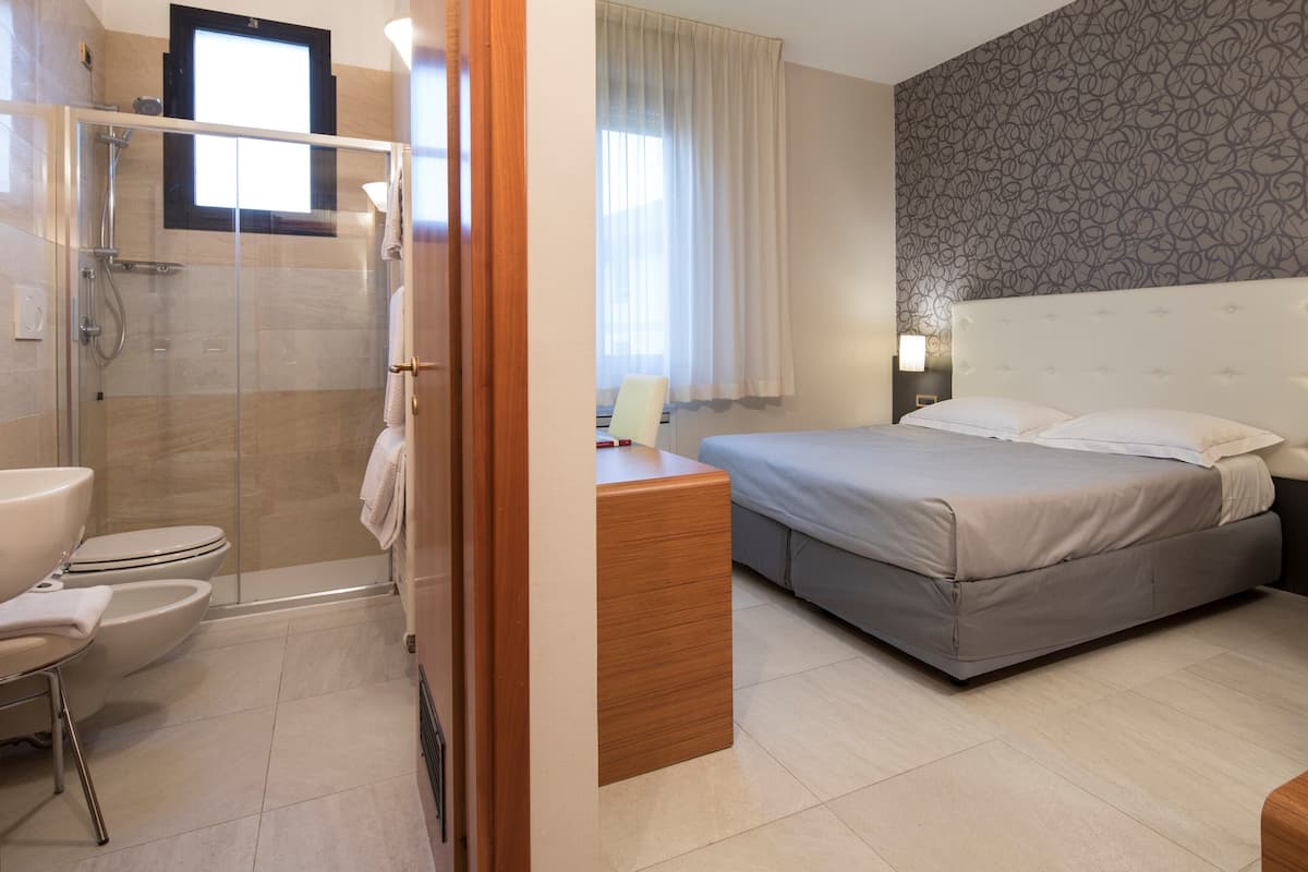 Une chambre d’hôtel équipée d’une douche, de toilettes, d’un lit, d’une table de chevet et d’une fenêtre avec des rideaux.