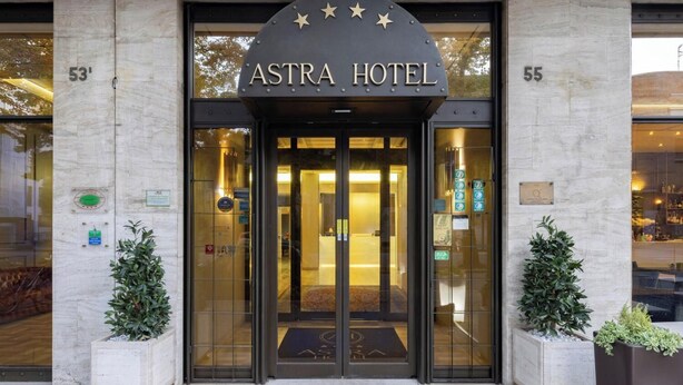 The entrance to the Astra Hotel with a star-shaped sign above the entrance, glass doors, and two potted plants on either side. - Hotel Astra Ferrara (Ferrara)
