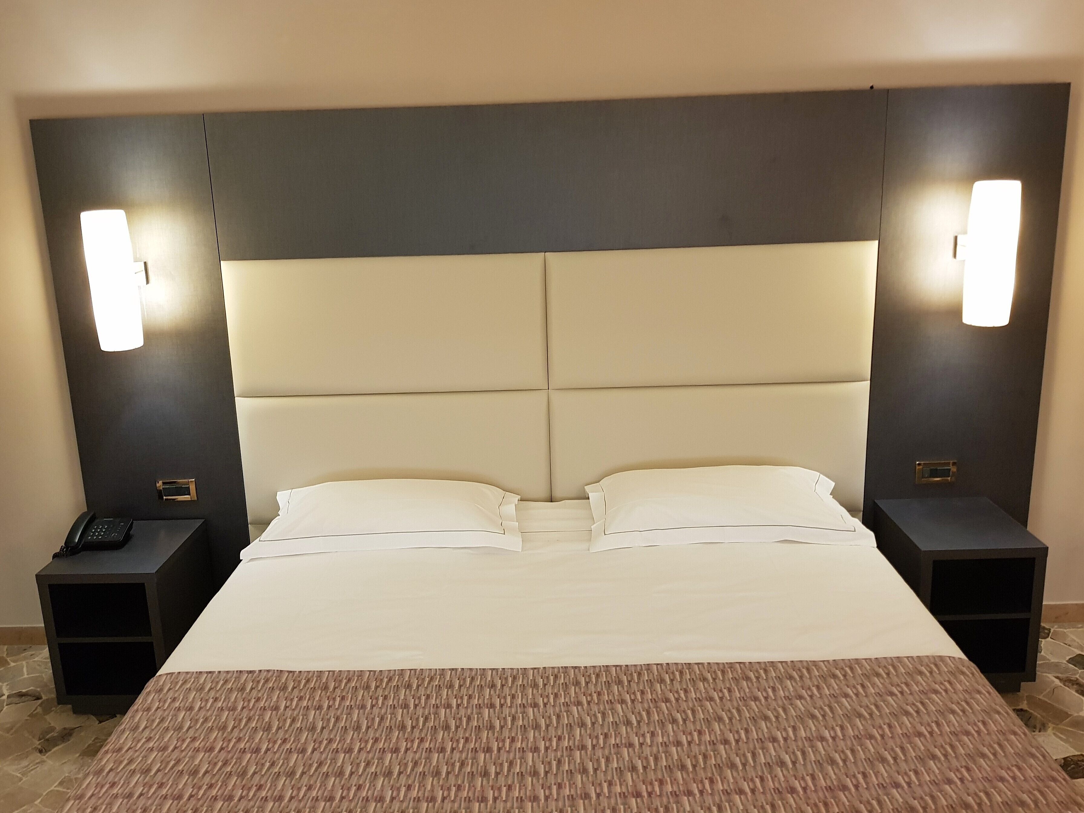 A hotel room with a large bed, two bedside tables, and wall-mounted lights.