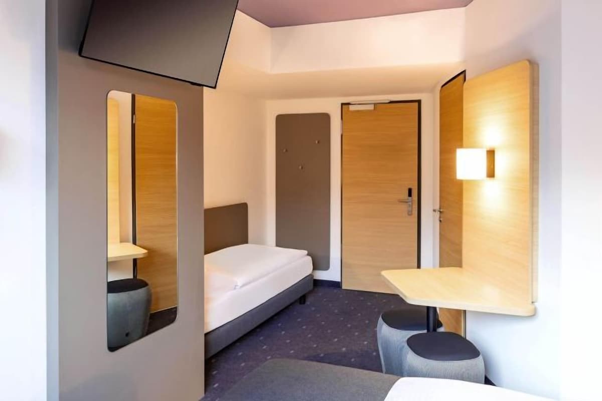 A hotel room with a bed, a desk, a chair, a mirror, and a TV.