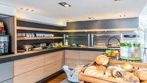 Moderni aamiaisbuffet, jossa on puiset kaapit, monipuolinen valikoima ruokia ja lasinen esillepanovitriini.