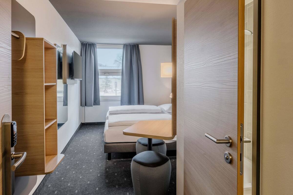 Una habitación de hotel con cama, escritorio, silla, televisor y armario.