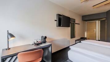 Habitación de hotel moderna con escritorio, silla, cama y televisor de pantalla plana montado en la pared.