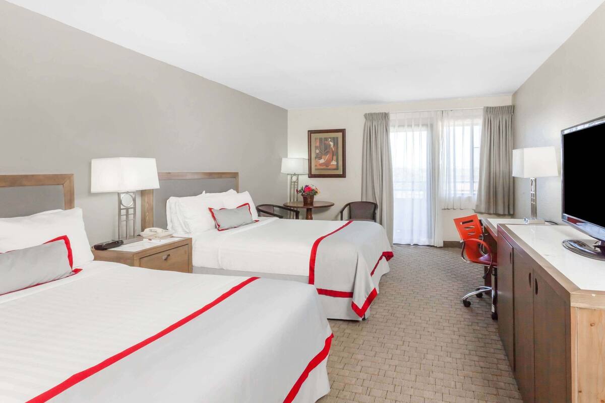 A hotel room with two beds, a desk, a TV, and a chair.
