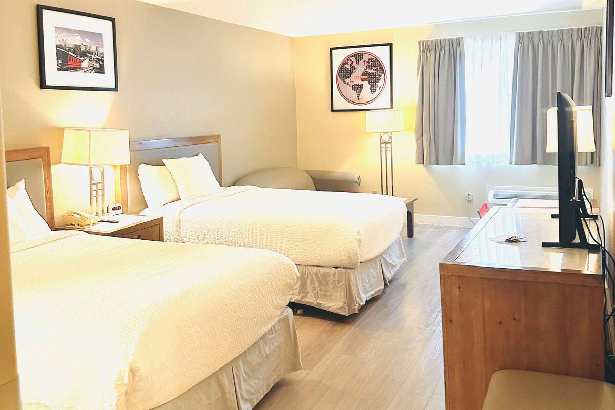 A hotel room with two beds, a desk, a chair, a TV, and two lamps.