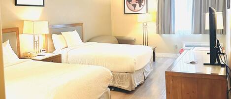 A hotel room with two beds, a desk, a chair, a TV, and two lamps.