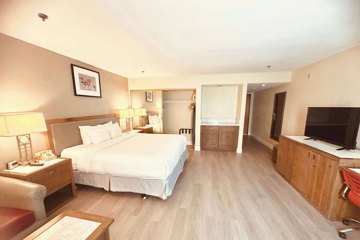A hotel room with a bed, bedside tables, a desk, a television, and a kitchenette area.