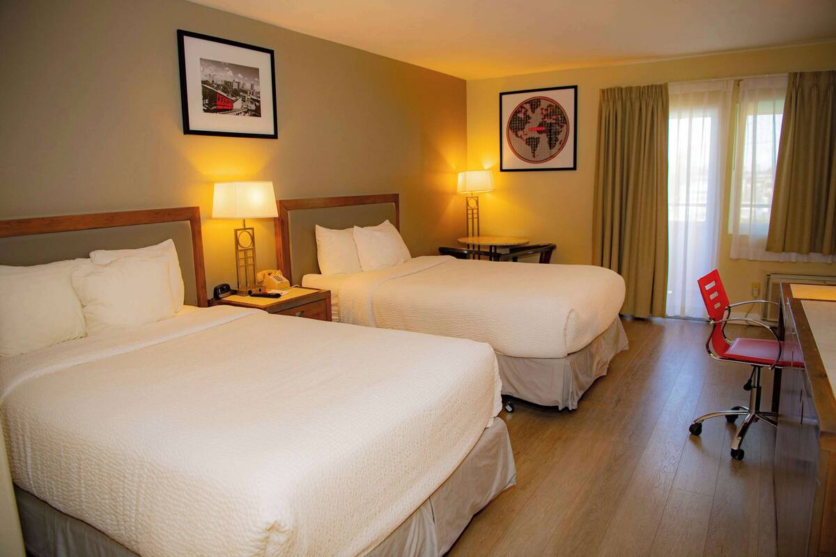 A hotel room with two beds, a desk, a chair, and two lamps.