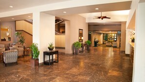 Eine geräumige Lobby mit hoher Decke, einer zentralen Treppe und einer Sitzecke mit Stühlen und Tischen.