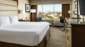 Ein Hotelzimmer mit einem grossen Bett, einem Schreibtisch mit Stuhl, einem Fenster mit Blick auf die Stadt und einem Flachbildfernseher.