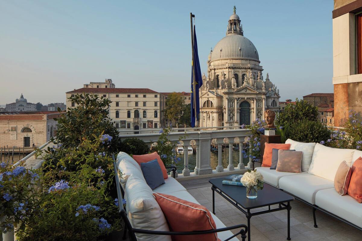 A terrace with a white sofa, a table, and a view of a historic building with a dome.