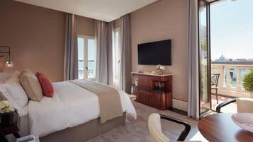 A hotel room with a large bed, a flat-screen TV, a dining area, and a balcony with a view.