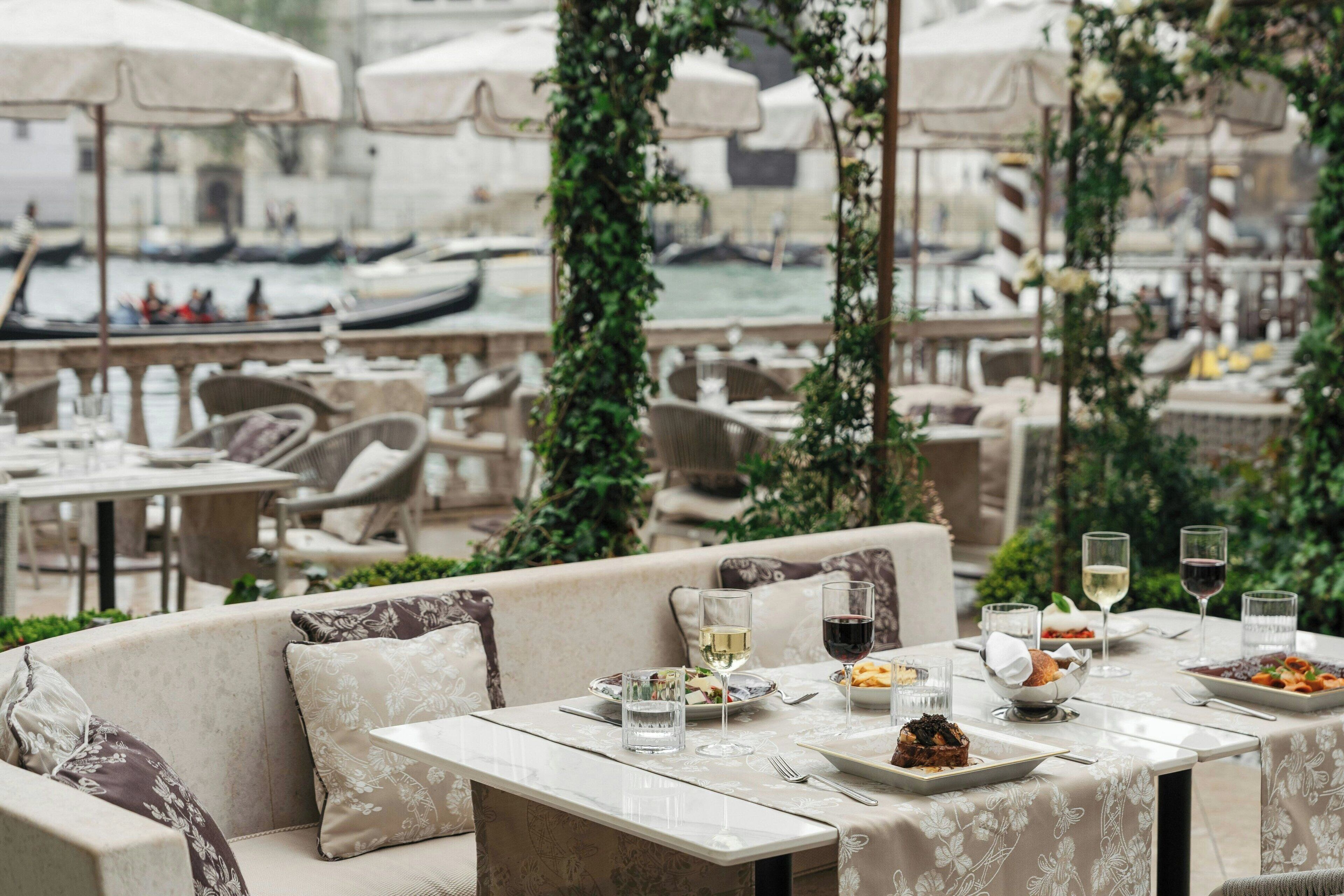 Un espace de restauration en plein air, avec des tables dressées pour le repas, donnant sur un canal où naviguent des bateaux.