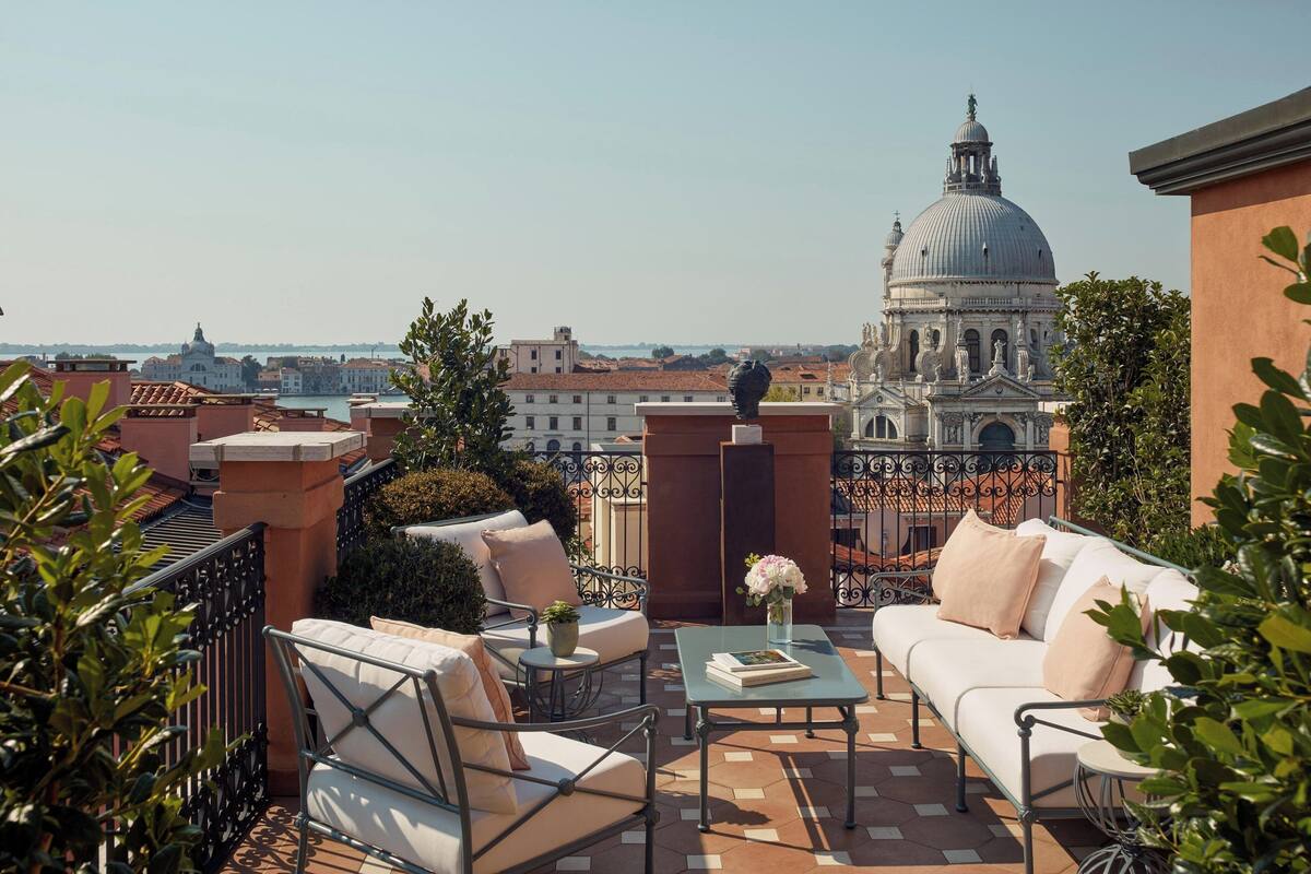 A terrace with a white sofa, a small table, and a view of a historic building with a dome.