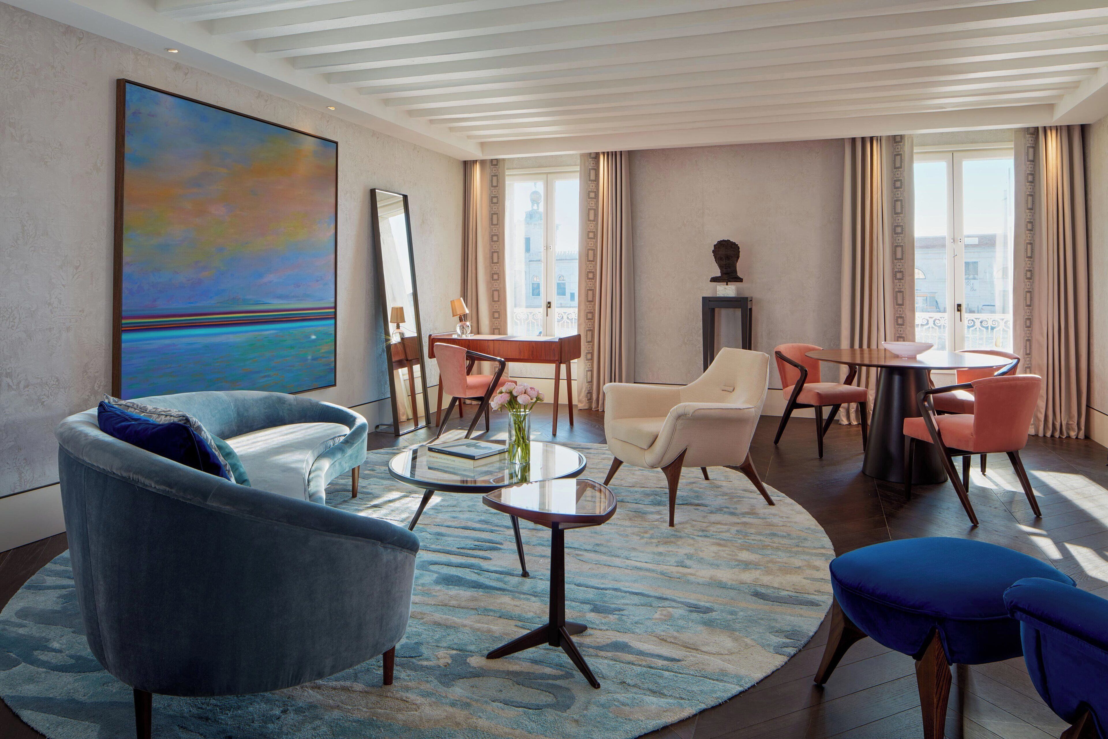 A modern hotel room with a large painting, a round coffee table, and a seating area with chairs and a sofa.