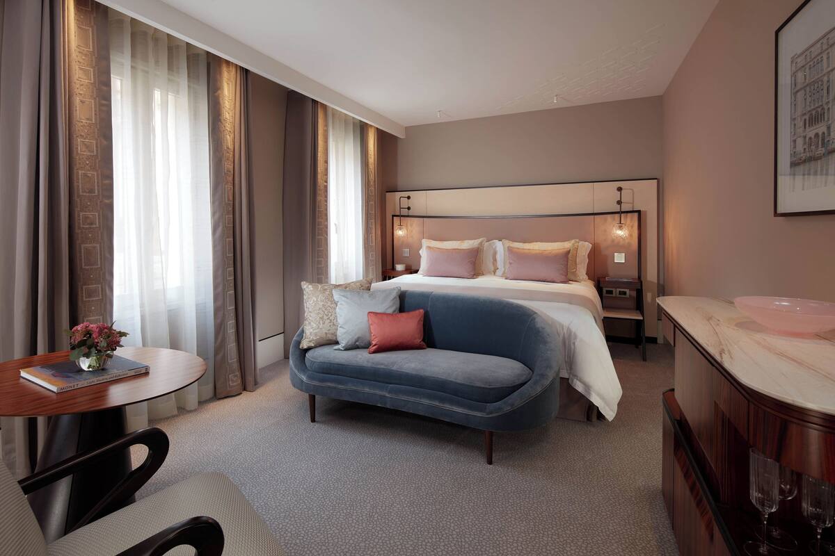 A hotel room with a bed, a sofa, a small table with a book, a bedside table, and a bathroom area.