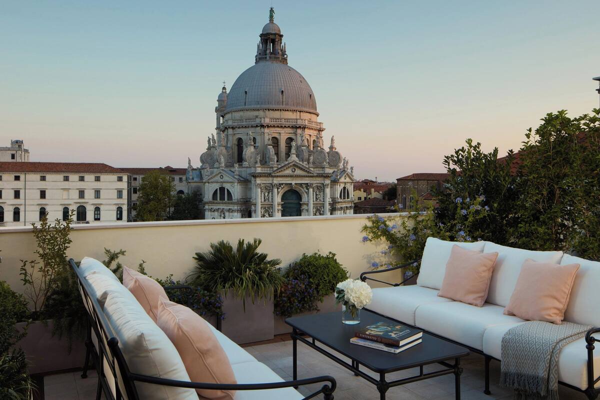 A terrace with a white sofa, a small table with books, and a view of a large historic building with a dome.