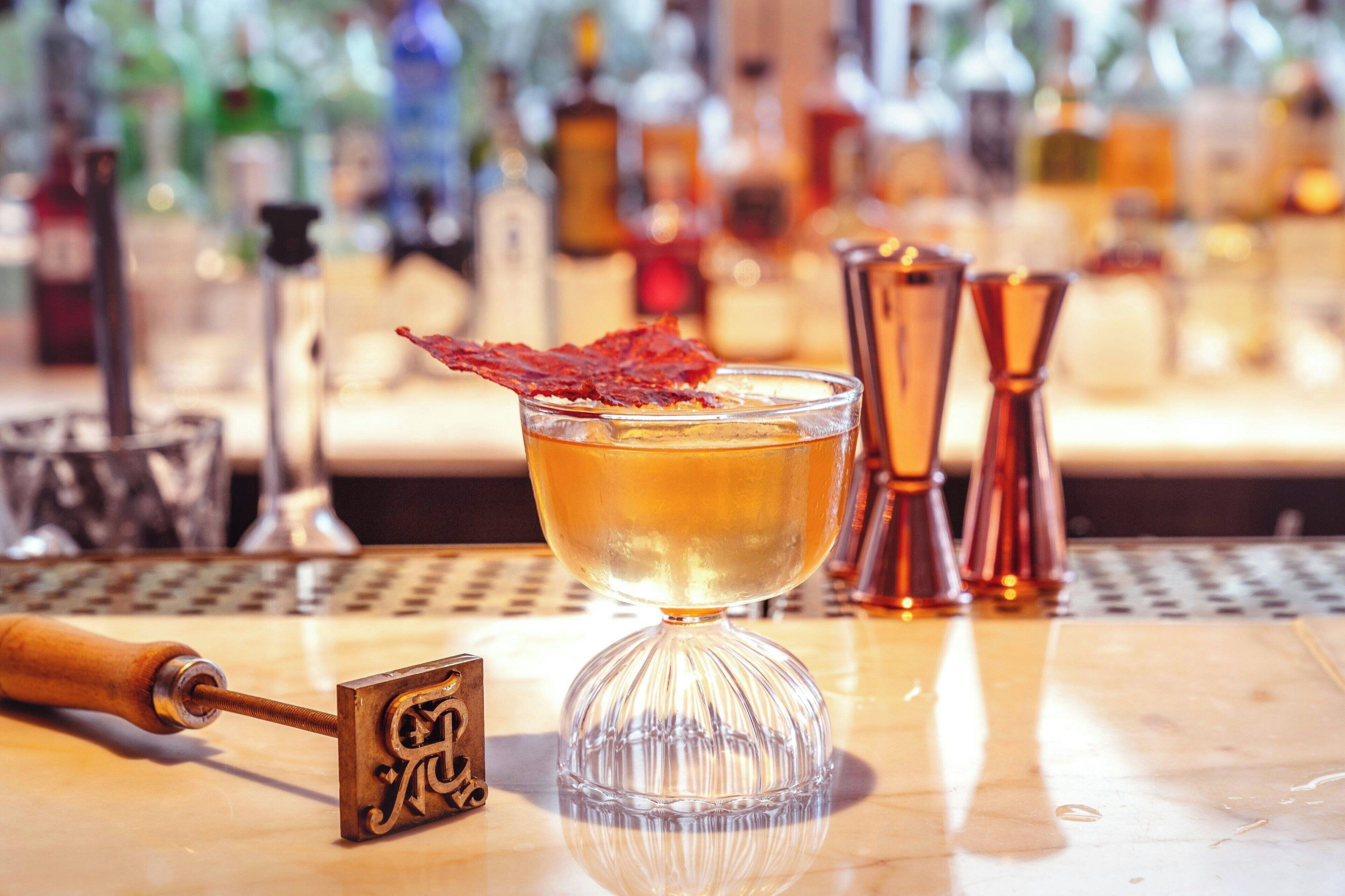 A bar setting with a cocktail glass, a cocktail shaker, and a bottle of liquor in the background.