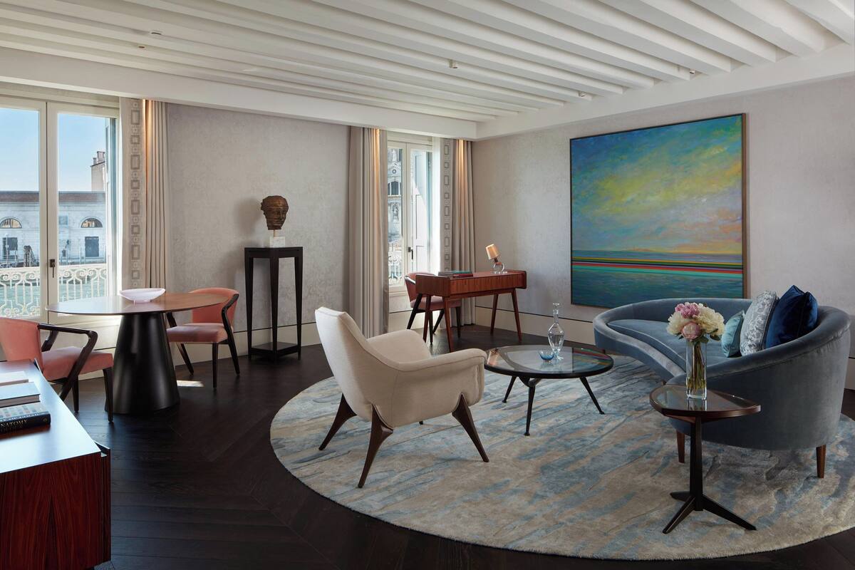 A modern living room with a round table, a sofa, and a coffee table. There is a painting on the wall and a view of the city through large windows.