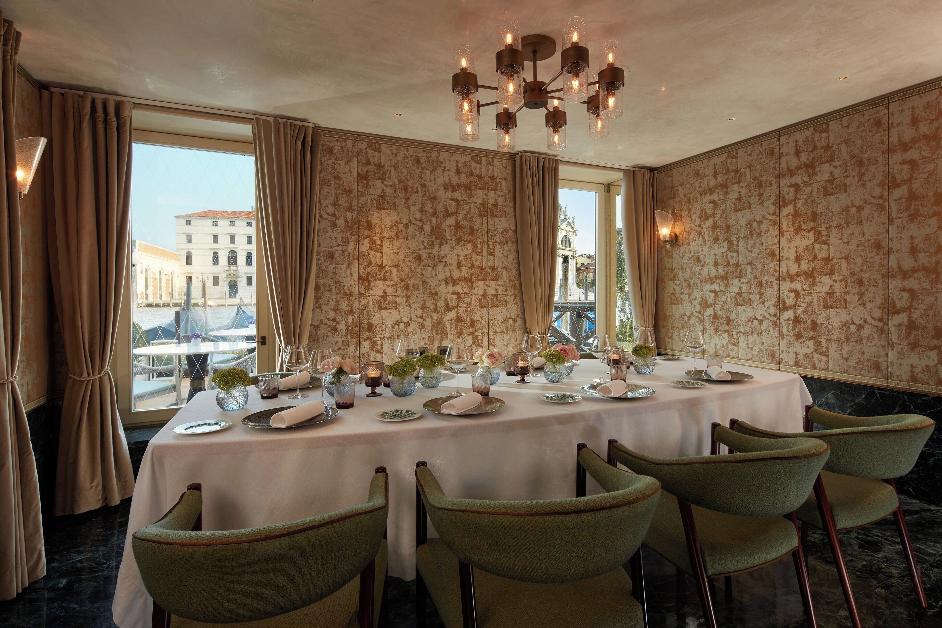 Une salle à manger avec une table dressée pour six personnes, de grandes fenêtres et un lustre.