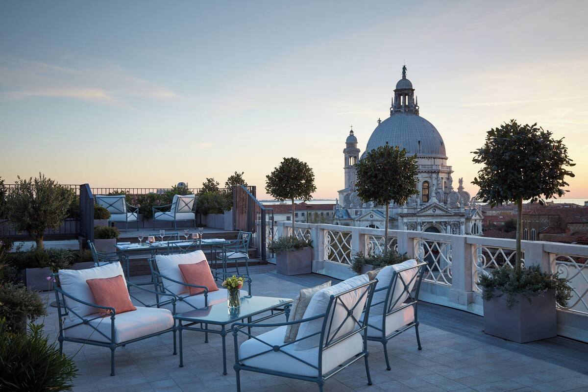 A rooftop terrace with outdoor seating, a view of a historic building, and potted plants.