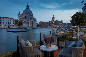 Una terraza con mobiliario de mimbre y vista a un edificio histórico al otro lado del río.