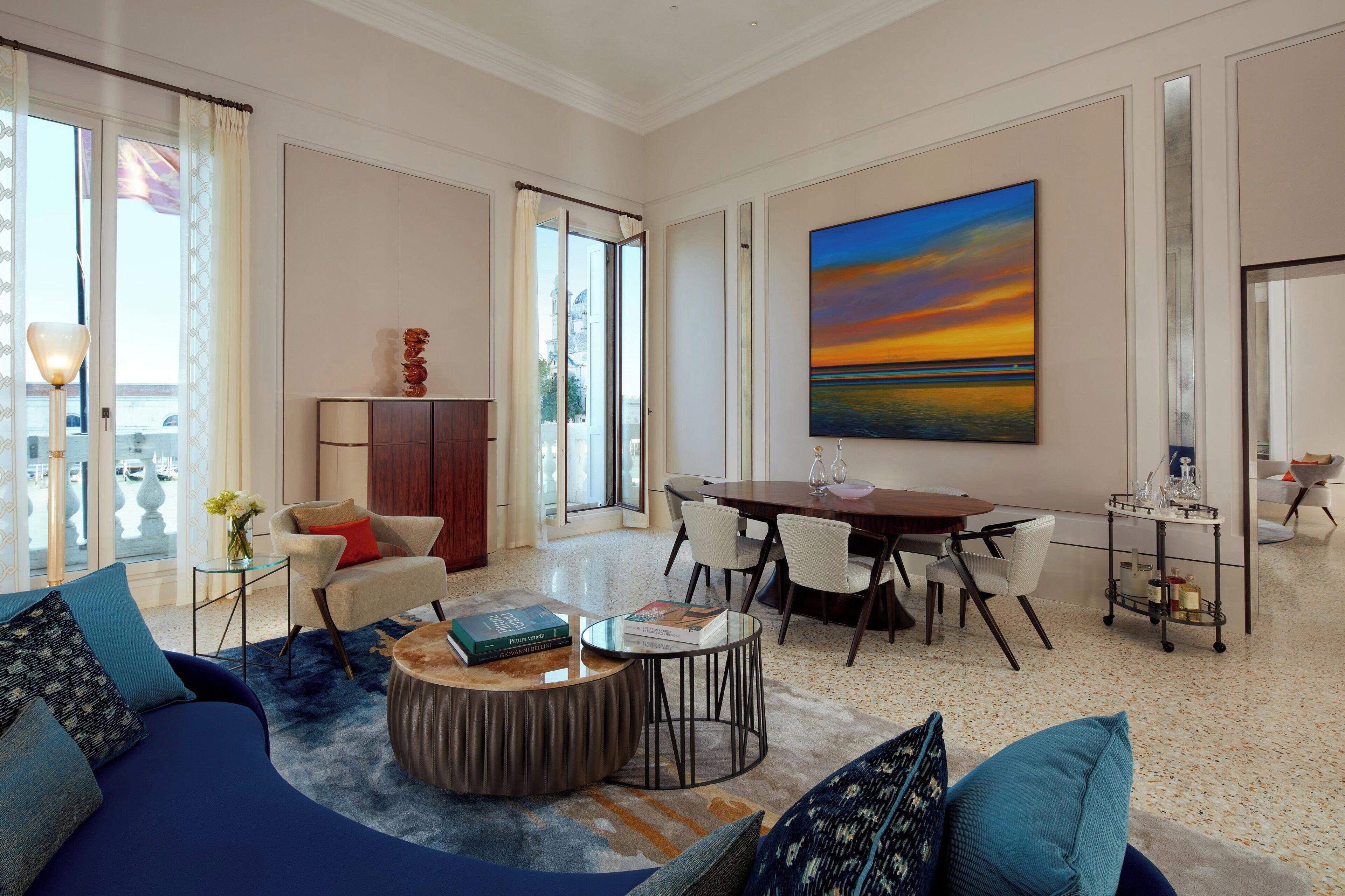 Een ruime woonkamer met een groot schilderij, een eethoek en een bank met decoratieve kussens.
